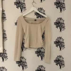 Beige långärmad topp från SHEIN - Snygg beige långärmad topp från SHEIN med bred, fyrkantig urringning. Modellen är croppad och har en stilren, enkel design som passar perfekt till jeans eller kjol. Tillverkad i mjukt och stretchigt material för en bekväm passform.