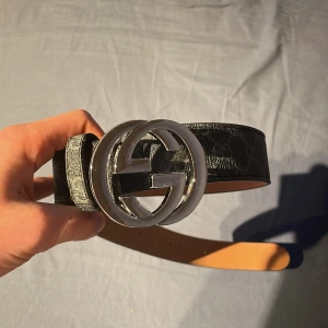 Svart Gucci skärp med silver GG-spänne - Säljer ett svart bälte från Gucci med ikoniskt dubbelt GG-spänne i silver. Bältet är gjort i äkta skinn och har diskret GG-mönster längs hela remmen. Prisset kan diskuteras vid snabbt köp 
