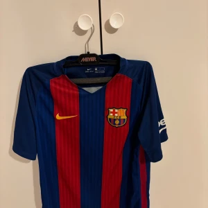FC Barcelona matchtröja  - Säljer en officiell FC Barcelona matchtröja från Nike i storlek M. Tröjan har klassiska blå och röda vertikala ränder, klubbmärke på bröstet, La Liga-märke på ärmen och Dri-FIT-material som andas. Perfekt för dig som älskar Barca och vill ha en ikonisk look.
