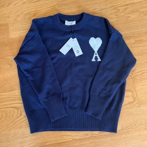Ami Paris Pullover Sweater - Snygg mörkblå stickad tröja från Ami Alexandre Mattiussi med vit hjärtlogga och A på bröstet. Tröjan har rund hals, ribbade muddar och är långärmad. Perfekt för dig som gillar stilrena och trendiga plagg. UTAN TAGS