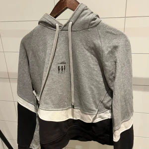 Grå och svart hoodie Neil Barrett - Snygg hoodie från Neil Barrett med huva och snörning. Tröjan har färgblock i grått, svart och vitt, samt en liten blixtdetalj på bröstet. Tillverkad i mjuk bomull, perfekt för chill dagar. Långärmad och loose fit för skön stil.
