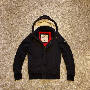 Kofta/cardigan från hollister - Riktigt snygg och limiterad svart kofta från hollister med dragkedja, knappar och fodrad luva. Storlek M. I mycket gott skick förutom att den är lite solblekt vilket syns på de 3 sista bilderna. Tveka inte på o skriva vid fler frågor!