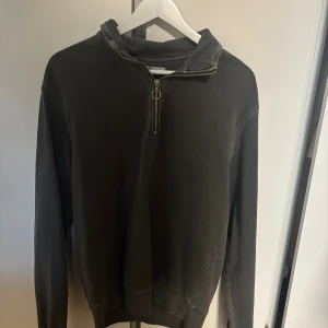 Mörkgrå half zip hoodie från Cubus - Säljer en mörkgrå hoodie med half zip-dragkedja och huva. Tröjan har långärmade ärmar och är tillverkad i mjukt bomullsmaterial. Perfekt för chill dagar och enkel att matcha med jeans eller joggers.