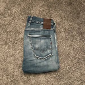 Replay Anbass - Snygga ljusblå Replay Anbass jeans med klassisk femficksdesign och brunt läderpatch bak. Jeansen har raka ben och coola slitningar för en avslappnad vibe. Perfekt passform och mjukt denimtyg som är skönt att bära hela dagen. W29 L32