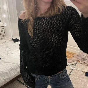 Svart stickad offshoulder tröja - Säljer en svart stickad tröja med offshoulder-design och grovt hålmönster. Tröjan har lång ärm och en loose passform som ger en chill vibe. Perfekt att styla med jeans eller kjol för en cool look. Fråga gärna om fler bilder eller mått!