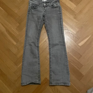 Grå bootcut jeans från Gina Tricot - Snygga grå jeans från Gina Tricot i bootcut-modell med klassiska fem fickor och silverfärgade knappar. Jeansen har normal passform och är tillverkade i mjukt denimtyg. Low rise och passar xs fast är i storlek 158