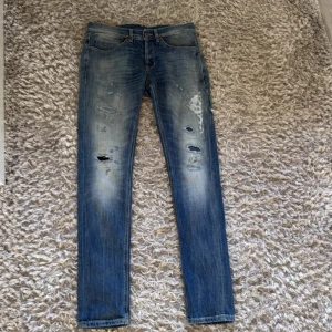 Dondup skinny jeans - Säljer ett par dondup jeans i blå tvätt med slitna detaljer och hål på framsidan. Modellen är skinny med smal passform och klassisk femficksdesign. Jeansen har en snygg faded effekt och är tillverkade i stretchigt denim för skön komfort.