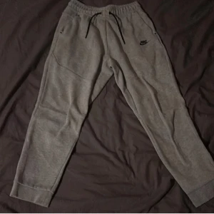 Grå mjukisbyxor från Nike XL - Grå mjukisbyxor från Nike i storlek XL, med svart snörning i midjan och diskret Nike-logga på vänster sida. Byxorna har elastisk midja, ribbade muddar vid benslut och praktiska sidofickor. Perfekt för chill eller träning.