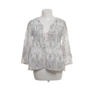 Mönstrad blus från Odd Molly - Supersöt blus från Odd Molly i vitt med ljusrosa och grått mönster. Blusen har långa ärmar, v-ringning med knyt och virkade detaljer längs halsringningen. Perfekt för dig som gillar boho-stil och mjuka material.