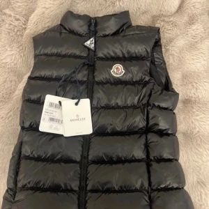 Svart dunväst från Moncler - Dunväst från Moncler. Har tyvärr inte något kvitto men har kvar lappar som äktehetsbevis. Även qr koden och triangeln på dragkedjan. Dock har triangeln löpte repor. Knappt använd 
