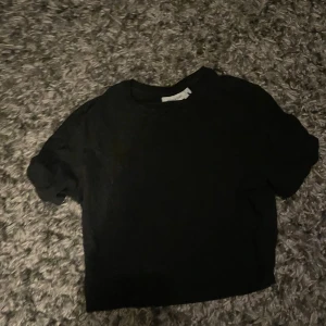 Svart croppad t-shirt från Weekday - Svart t-shirt från Weekday i croppad modell med rund hals och korta ärmar. Tillverkad i mjuk bomull som känns skön mot huden. Enkel och clean design som funkar till allt, perfekt för dig som gillar minimalistisk stil.