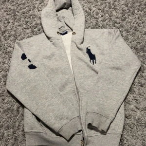 Grå full zip Ralph Lauren  - Snygg grå hoodie från Ralph Lauren med dragkedja, stor marinblå logga på bröstet och siffra 3 på ärmen. Mjuk insida och huva med metallöljetter. Perfekt för chill dagar och för att öka din stil alla dagar. För mer info skicka. Pris kan diskuteras 