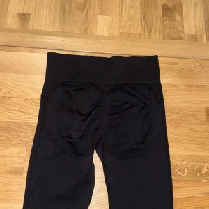 Svarta högmidjade leggings - Använt några gånger, dem har blivit små för mig så Säljer ett par svarta leggings med hög midja och tight passform. De har meshdetaljer längs sidorna och runt rumpan för extra ventilation och stil. Perfekta för träning eller chill, tillverkade i stretchigt syntetmaterial som sitter skönt mot kroppen.