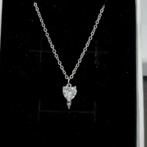 Halsband  - Ett stilrent halsband i silverfärg med en tunn kedja och ett gnistrande hjärta som hänge. Hänget är dekorerat med en klar kristall som fångar ljuset snyggt. Perfekt accessoar för att lyfta din look med en touch av romantik.