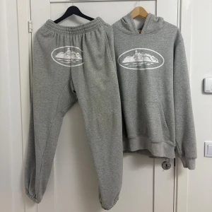 🩶 Corteiz Tracksuit (Grå) – Hoodie & Byxor – Storlek M - Mjuk grå tracksuit från Corteiz med matchande tryck på både hoodie och joggers. Perfekt passform och hög komfort. Storlek: M