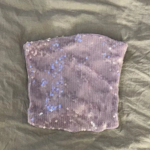 Ljuslila paljett-tubtopp Gina Tricot - Superfin ljuslila tubtopp från Gina Tricot, täckt med paljetter. Toppen är bandeau-modell och sitter tight mot kroppen. Dragkedja på baksidan. Helt ny, aldrig använd 