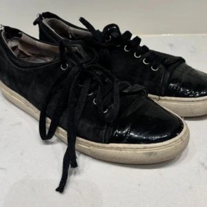 Svarta sneakers med lackad tå - Svarta sneakers med snygg lackad tå och klassisk vit sula. Skorna har snörning och en mix av material med både mockaliknande och glansiga detaljer. Perfekta för dig som gillar en stilren men ändå lite edgy look. Det är inte lika slitet i verkligheten!
