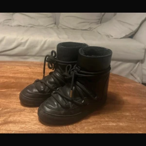Svarta Inuikii boots i full leather - Pris kan diskuteras. Säljer ett par svarta Inuikii boots i full leather modellen med grova snören och guldfärgade detaljer. Skorna är fodrade för extra värme och en inbyggd kilklack. Perfekta för kalla dagar och har en riktigt chunky vibe. 