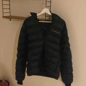 Svart dunjacka från Peak Performance - Säljer en svart dunjacka från Peak Performance med huva och dragkedja framtill.  Jackan är i bra skick och bara andvänds lite förra vintern men nu blivit för liten  skicket skulle jag säga 8/10 bara ett litet hål på ärmen fast de är lagat