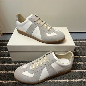 Maison Margiela vit/grå - Maison Margiela sneakers i vitt skinn och ljusgrå mocka med beige snörning och klassisk gummisula. Snygg retrostil med rund tå och platt sula. Priset kan diskuteras vid snabb affär 