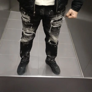 Supply & Demand svarta jeans med slitningar - Svarta jeans från Supply & Demand med coola slitningar och färgstänk över hela byxorna. Modellen har raka ben och flera rejäla hål och trasiga detaljer på framsidan för en edgy streetstil. Jeansen har klassisk femficksdesign och är tillverkade i jeansmaterial. Storlek 32 sitter perfekt på mig använt dom i 2 månader  helt och hållet rena o fräscha o fortfarande som nya . Säljes för 500