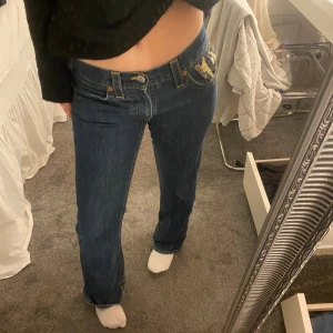 True Religion jeans med gul detalj - Säljer ett par blå jeans från True Religion med  detaljer på bakfickorna och snygga kontrastsömmar. Dem är för små för mig och ser därför väldigt tajta ut men är inte det om den passar som dem ska. Hör av er för fler bilder eller frågor🤍