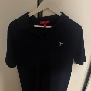 Mörkblå kortärmad skjorta från Guess  - Snygg mörkblå kortärmad skjorta från Guess med klassisk krage och diskret logga på bröstet. Skjortan har en stilren look och är perfekt för dig som gillar enkel men trendig stil.