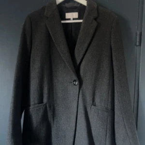 Snygg grå ullkappa från Brothers & Sisters butiken - Elegant och tidlös kappa i mjuk ullblandning (60% ull, 40% polyester) med slätt foder för skön passform. Perfekt för både vardag och fest! Klassisk siluett, hög kvalitet och stilren design.  I mycket fint skick  redo att värma dig med stil i höst! 🍂 