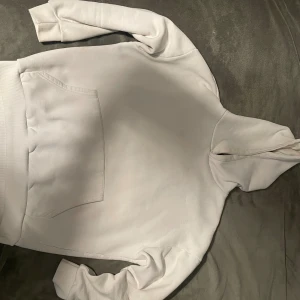 Vit hoodie - Snygg vit hoodie med klassisk huva. Tröjan har ribbade muddar vid ärmslut och nederkant, samt en relaxed passform. Perfekt för chill dagar och enkel att matcha med jeans eller mjukisbyxor.