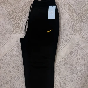 Nike NOCTA svarta mjukisbyxor - Helt nya svarta mjukisbyxor från Nike NOCTA i storlek S med gul logga och detaljer. Byxorna har dragsko i midjan. Tillverkade i mjukt material för maximal komfort och stilren look. Byxorna är oanvända och taggarna sitter kvar.