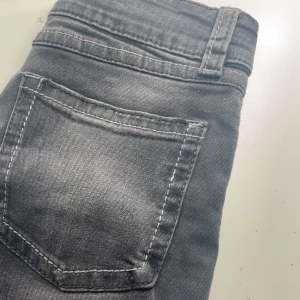Grå bootcut jeans från Ginatricot - Snygga grå jeans från Ginatricot med bootcut passform och klassisk femficksdesign. Jeansen har kontrastsömmar, dubbla knappar i midjan och är tillverkade i mjukt denimtyg. Perfekt för dig som gillar en lite retro vibe och vill ha ett par jeans med schysst siluett.