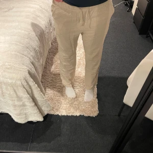 Beiga linnebyxor med snörning - Snygga beiga linnebyxor med avslappnad passform och snörning i midjan. Byxorna har raka ben och fickor fram . Perfekta för en chill och stilren look, passar till sneakers eller sandaler.