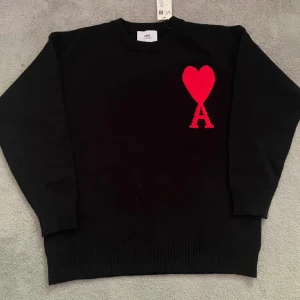  tröja från Ami - Svart stickad tröja från Ami med rött hjärta och bokstaven A broderat på bröstet. Rund hals och ribbade muddar vid ärmslut och nederkant. Perfekt för dig som gillar stilrena detaljer med en twist.