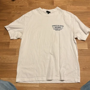 Vit loose fit t-shirt H&M Enrico & Sons - Vit t-shirt från H&M i loose fit med tryck fram och stort färgglatt tryck bak med texten Enrico & Sons, New York City och en gul truck. Skön bomullskvalitet och klassisk rund hals. Perfekt för dig som gillar streetstyle och coola prints.