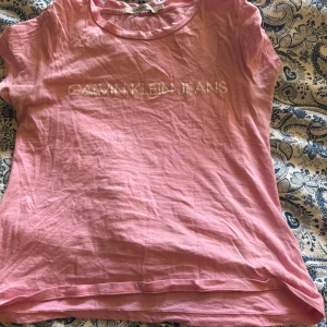 Rosa Calvin Klein Jeans t-shirt - Snygg rosa t-shirt från Calvin Klein Jeans med logga broderad framtill. Klassisk rund halsringning och korta ärmar. Tillverkad i mjuk bomull som känns skön mot huden. Perfekt för en avslappnad och trendig look.