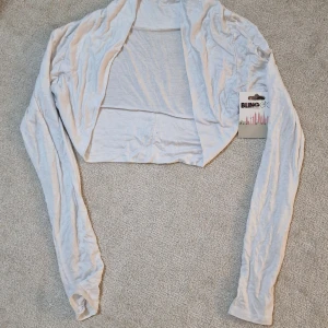  kofta från Blingetc - Supermjuk och tunn vit kofta från Blingetc. Modellen är croppad och öppen framtill med långa ärmar. Perfekt att slänga över ett linne eller klänning för en chill look. Materialet är lätt och stretchigt, vilket gör den riktigt skön att bära.