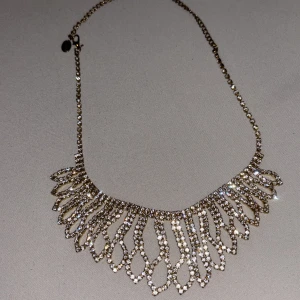 Glittrigt guldhalsband med strass - Supersnyggt halsband i guld med glittrande strass-stenar. Kedjan är tunn och smycket har ett unikt, droppformat mönster som ger en lyxig känsla. Perfekt för att lyfta vilken outfit som helst med extra bling.