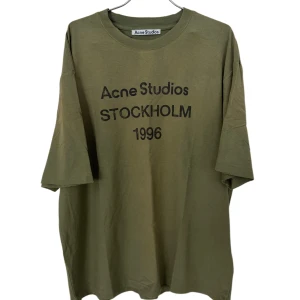 Olivgrön Acne Studios t-shirt Stockholm unisex storlek S/M - Olivgrön t-shirt från Acne Studios med tryck 'Stockholm 1996' på bröstet. Modellen är loose fit med korta ärmar och rund hals. Materialet är mjuk bomull och t-shirten har en clean, minimalistisk vibe som passar streetwear och casual stil.