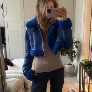 Blå croppad teddyjacka / skinnjacka  - Säljer denna ascoola croppade blå skinnjackan från Stand Studios. Den är fodrad vilket gör att den även ger värme utöver att bidra med den perfekta färgklicken till din outfit. Jackan är i nyskick och nypriset ligger på runt 6500kr.  