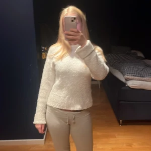 Vit stickad tröja med hög hals - Mysig vit stickad tröja med hög hals och långärmad design. Tröjan har en lite croppad passform och ribbade muddar vid ärmslut och nederkant. 