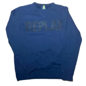 Blå sweatshirt från Replay - Snygg blå sweatshirt från Replay med stort guldigt tryck över bröstet. Tröjan har rund hals och långa ärmar, perfekt för dig som gillar stilrena och coola plagg. Materialet är mjuk bomull som känns skönt mot huden.