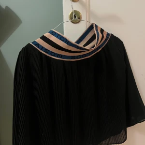 Svart plisserad kortkjol från Scotch & Soda - Svart plisserad kortkjol från Scotch & Soda Maison Scotch med bred, elastisk midja i beige, svart och blått med logotyp.