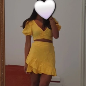 Gul volangkjol & topp med omlott-look  - Säljer en kort gul kjol & topp med volangkant och omlott-design. Kjolen har en mjuk och lätt känsla, perfekt för varma dagar. Den har en feminin och trendig look med volanger som ger extra rörelse. Passar dig som gillar färgglada och somriga outfits.