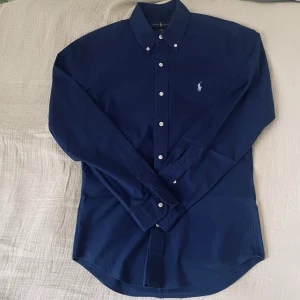 Mörkblå skjorta från Ralph Lauren - Riktigt clean skjorta från Ralph Lauren i mörkblått med ikoniska loggan på bröstet. Button-down modell som sitter sjukt snyggt både uppknäppt och knäppt.  📏 Storlek: S (men passar M) ✨ Skick: I princip nyskick  🧵 Material: Bomull, riktigt skön och lätt att bära.        ✅ Pris kan diskuteras
