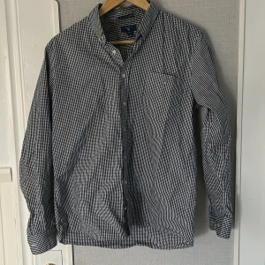 Rutig skjorta från GANT, svartvit - Snygg svartvit rutig skjorta från GANT med klassisk button-down krage och bröstficka. Skjortan är långärmad och har knappar hela vägen framtill. Tillverkad i mjuk bomull, perfekt för en clean och stilren look. Skojrtan är bra i skick de bara den är inte strykt. Den passar s 