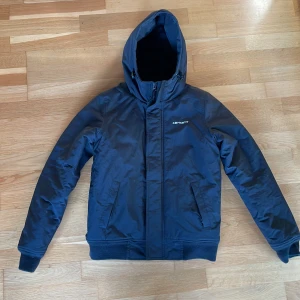 Svart  jacka  från Carhartt XS - Snygg svart jacka från Carhartt med huva och dragkedja framtill. Jackan har två sidofickor med dragkedja och ribbade muddar vid ärmslut och nederkant. Svarar gärna på frågor! 😊