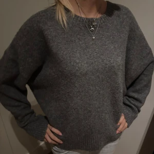 Grå stickad tröja från Zara - Mysig grå stickad tröja från Zara i storlek M. Tröjan har en klassisk rund halsringning, långa ärmar och ribbade muddar vid ärmslut och nederkant. Perfekt för lager-på-lager och chill dagar.