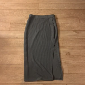 Mörkgrå ribbad långkjol från Boture - Säljer en mörkgrå, ribbad långkjol från Boture i storlek S. Kjolen har en smal passform och en snygg slits på sidan som ger extra edge. Tillverkad i mjuk och stretchig polyesterblandning för en bekväm känsla hela dagen.