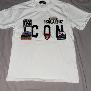 Dsquerd2 T-shirt - Vit t-shirt från Dsquared2 med stora svarta 'ICON'-bokstäver och flera färgglada broderade patches framtill. Klassisk passform, rund hals och korta ärmar. Materialet är mjuk bomull och loggan finns även tryckt i nacken.