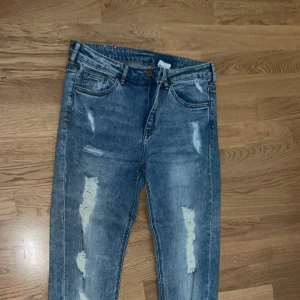Blå slitna skinny jeans från H&M - Säljer ett par blå skinny jeans med slitningar och snyggt tvättad look. Jeansen har klassisk femficksdesign, normal midja och är tillverkade i stretchigt denim för en tight passform. Perfekta för dig som gillar en trendig och avslappnad stil.